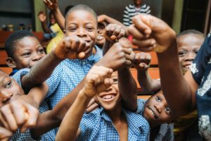 Group of smiling African children showing unity with raised fists in a classroom setting.